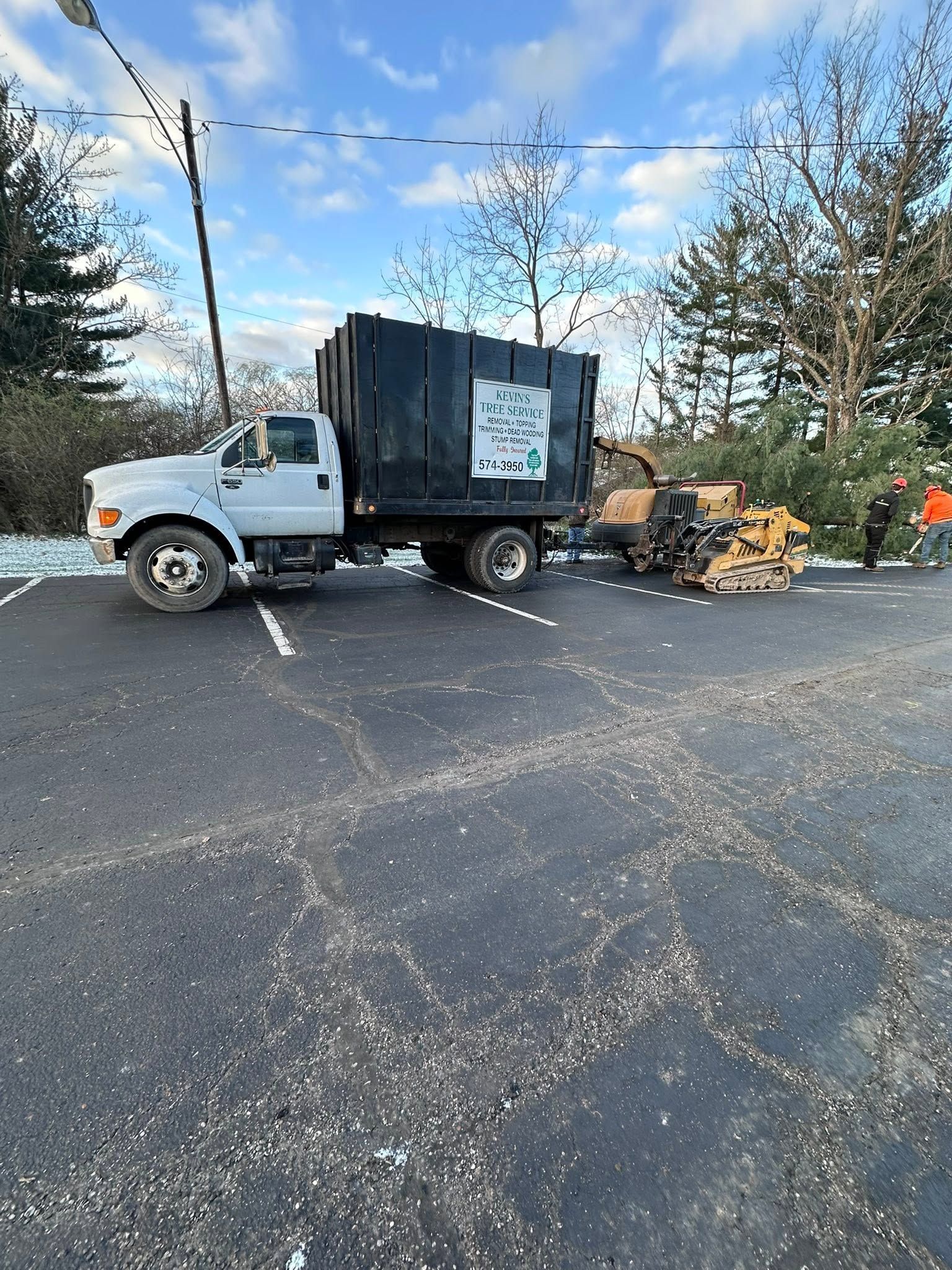 White utility truck with black equipment box and mower on roadside, with worker in orange vest nearby.