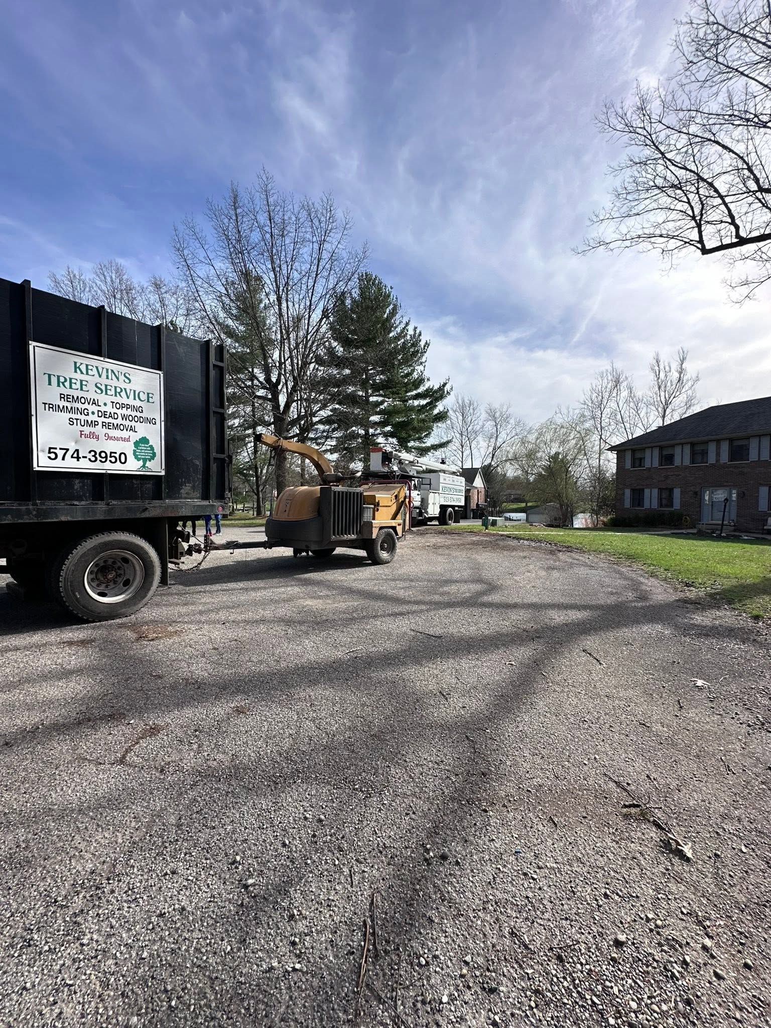 Gravel driveway with a moving truck, trees, and a brick building under a blue sky