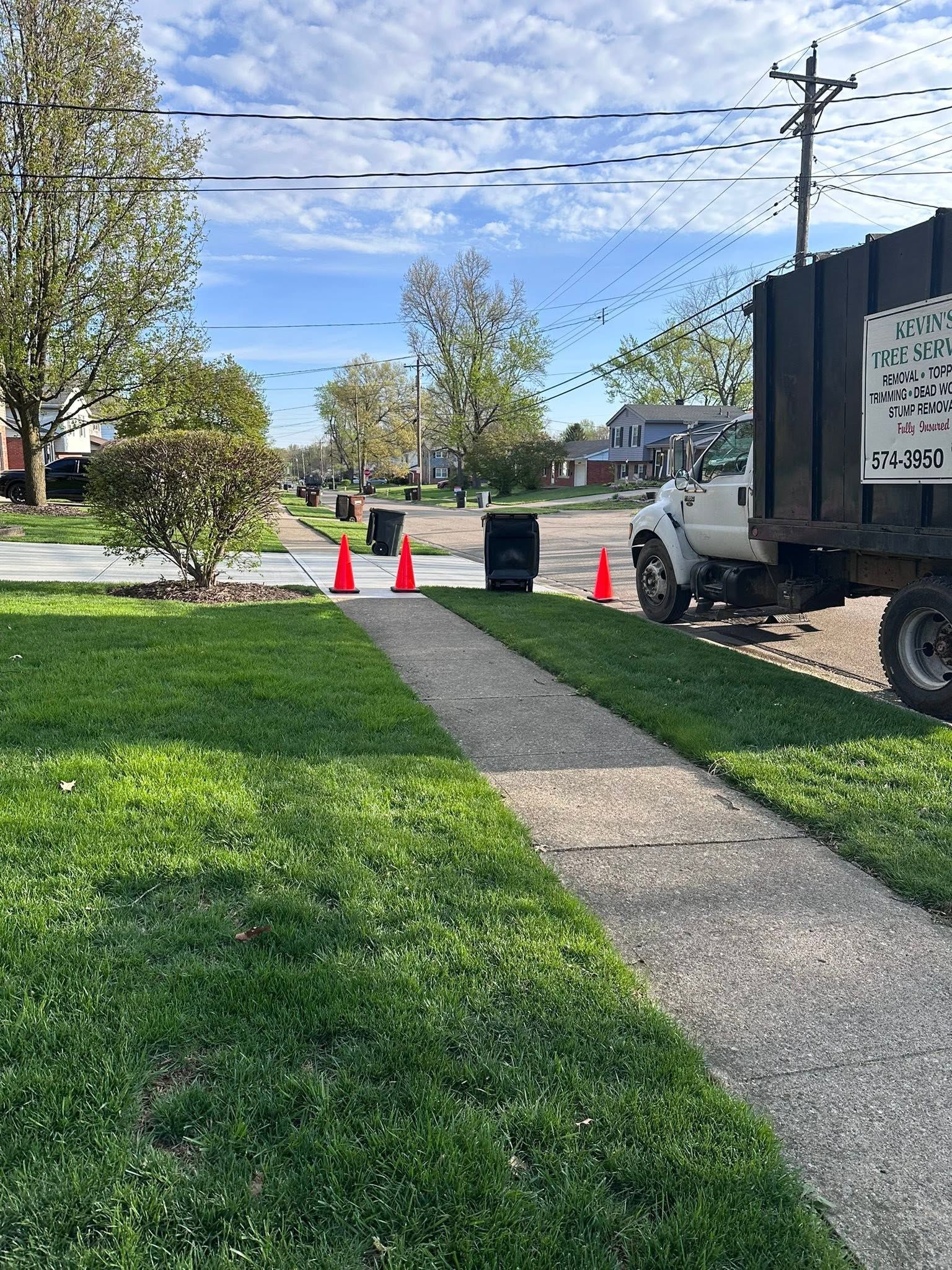 Trash truck on a suburban street beside a sidewalk, with orange cones marking the area.