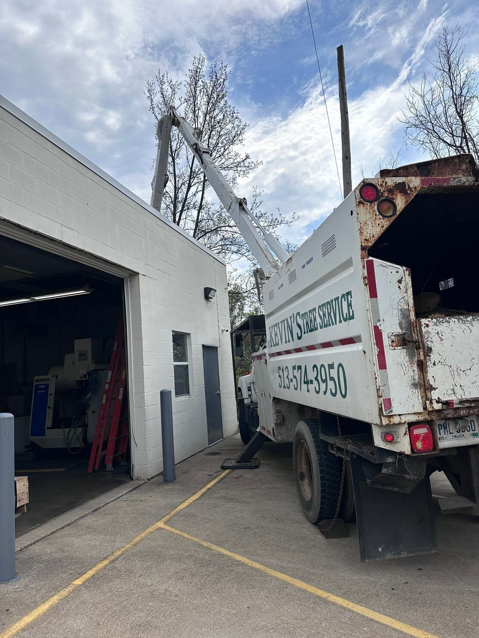 White utility truck parked beside an open garage in an industrial yard, with a metal bin and yellow lines.