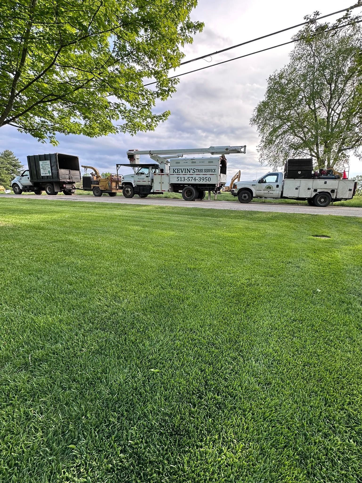 Utility trucks parked beside a road with green grass and trees in the foreground