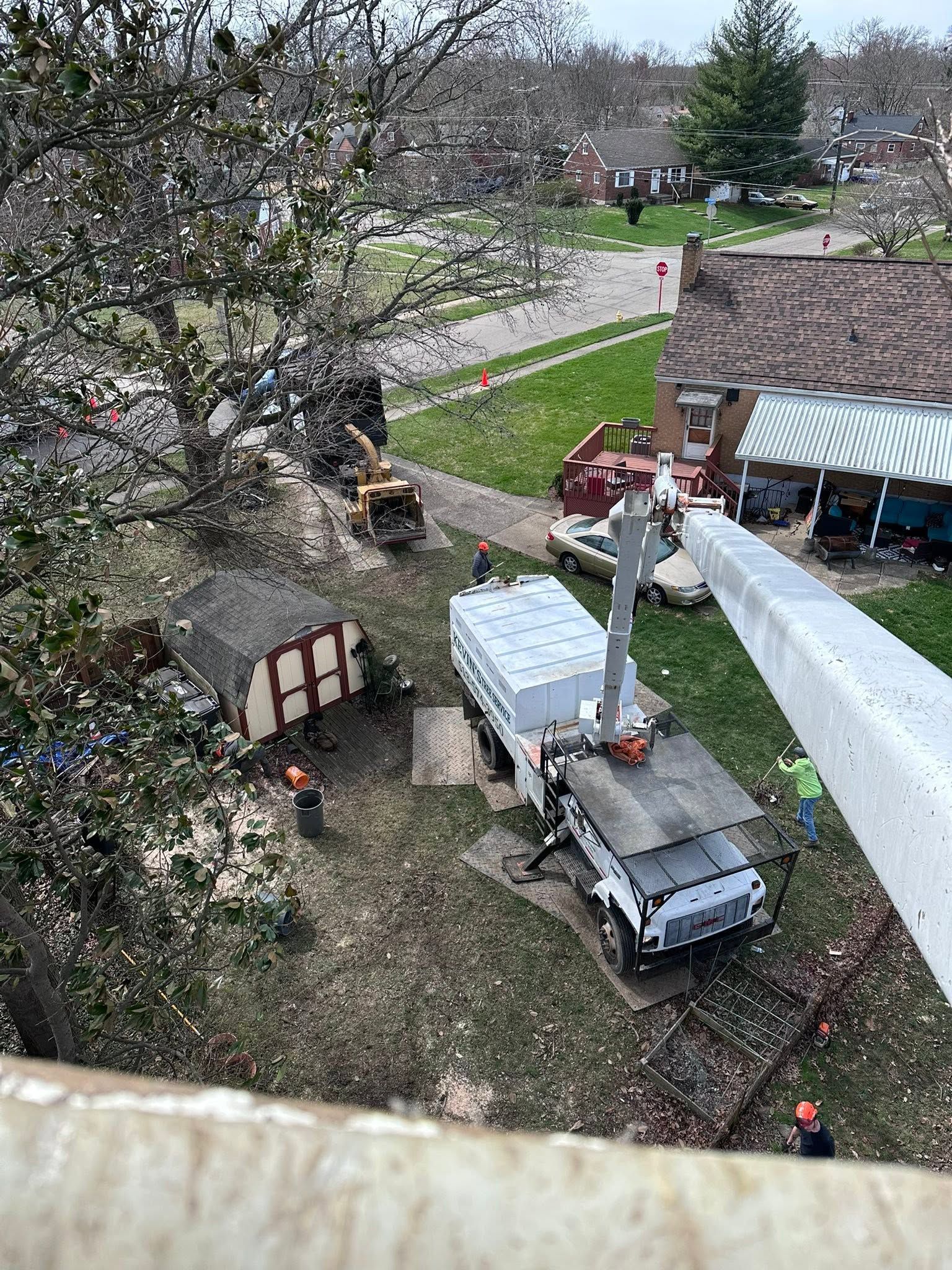 Aerial view of a backyard with a truck, white trailer, and workers near a house and blossoming trees.