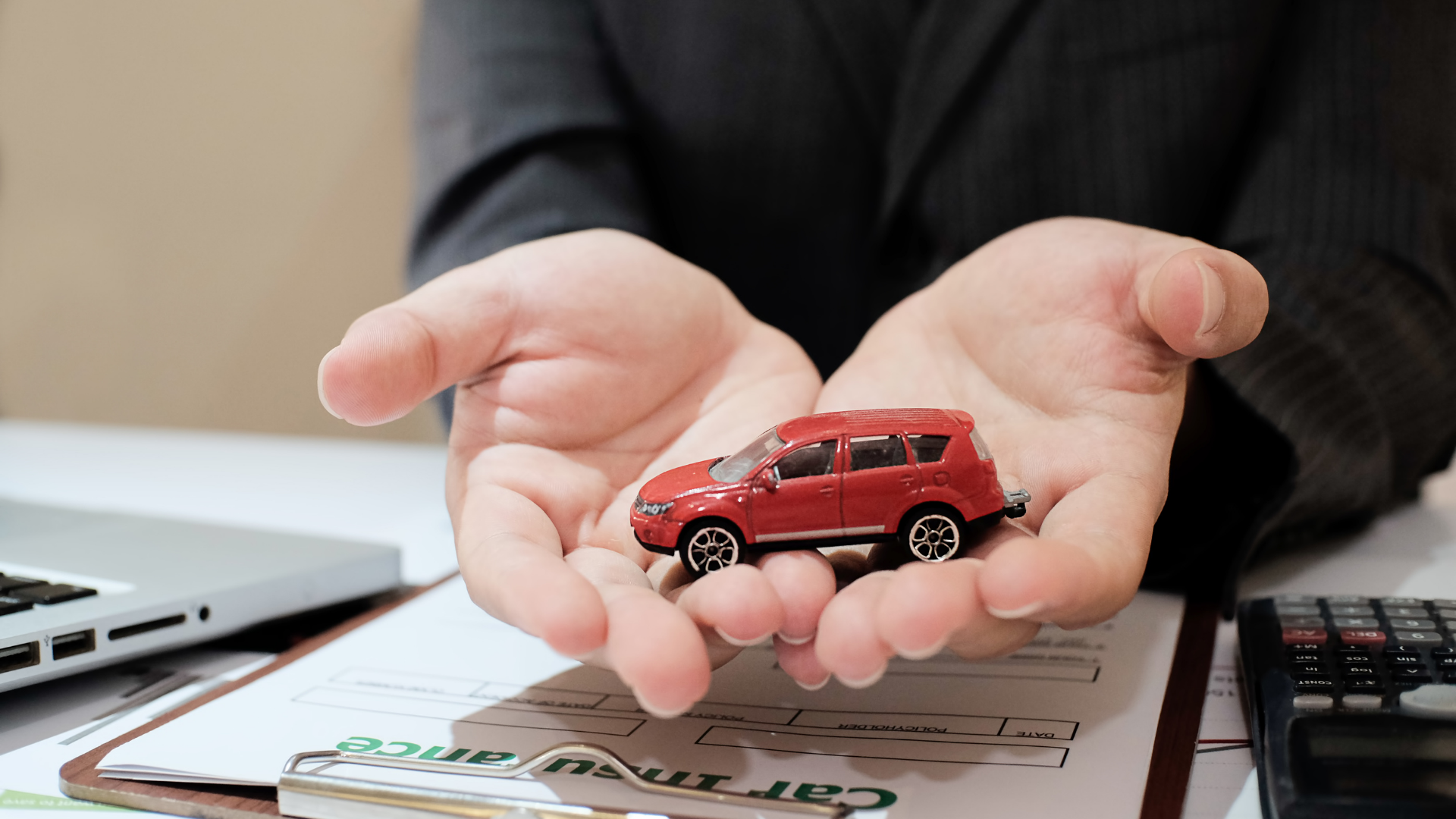 A person holding a small red car model in their hands, symbolizing the importance of protecting your new car with insurance.