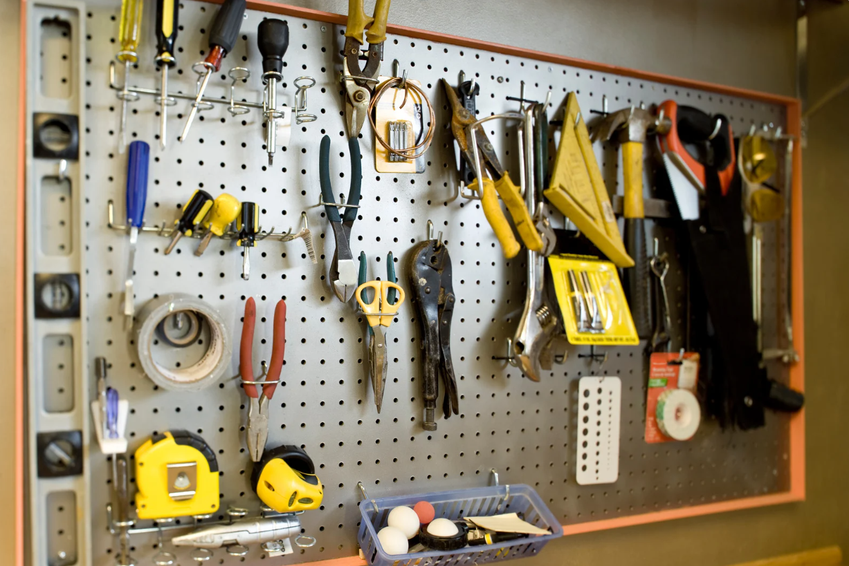 Tools organized on a pegboard in a workshop; includes pliers, screwdrivers, tape measure, hammer, and gloves.