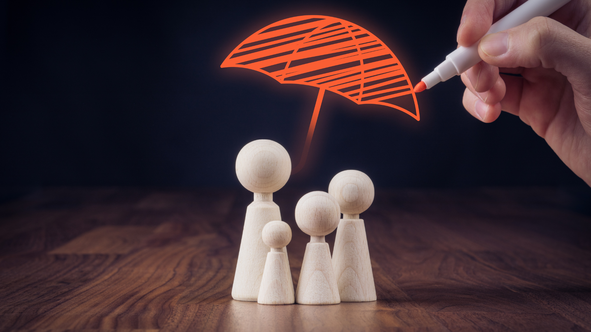 A hand drawing an umbrella above wooden figurines representing a family, symbolizing insurance cover