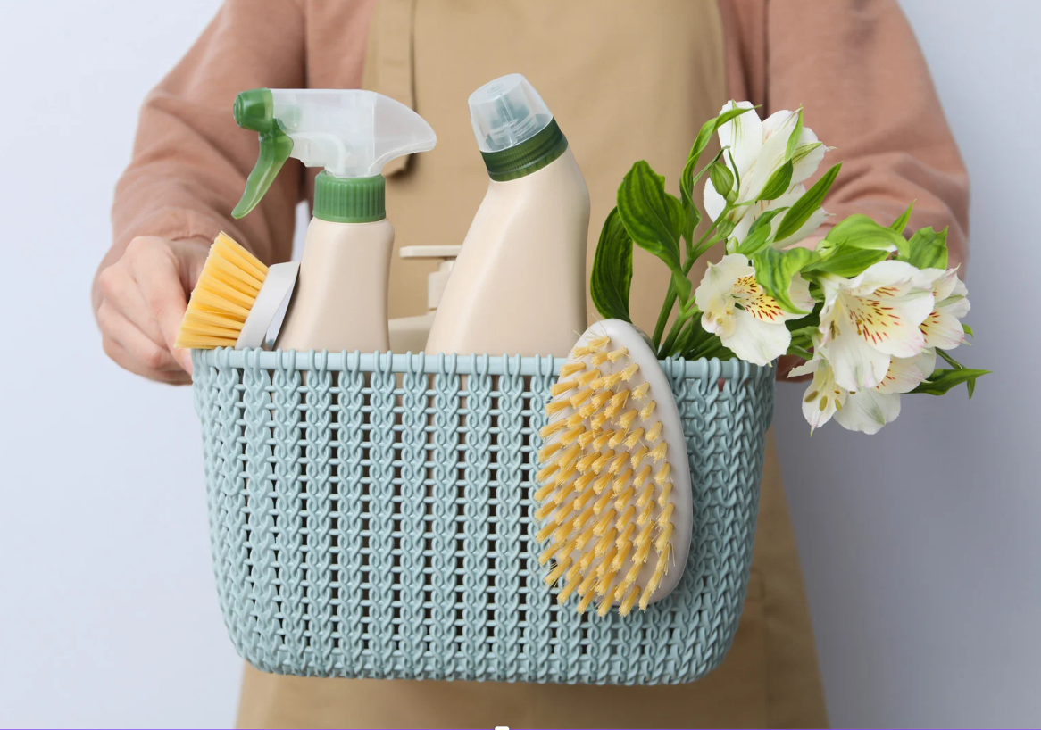 Person holding a blue basket filled with cleaning supplies and white flowers.