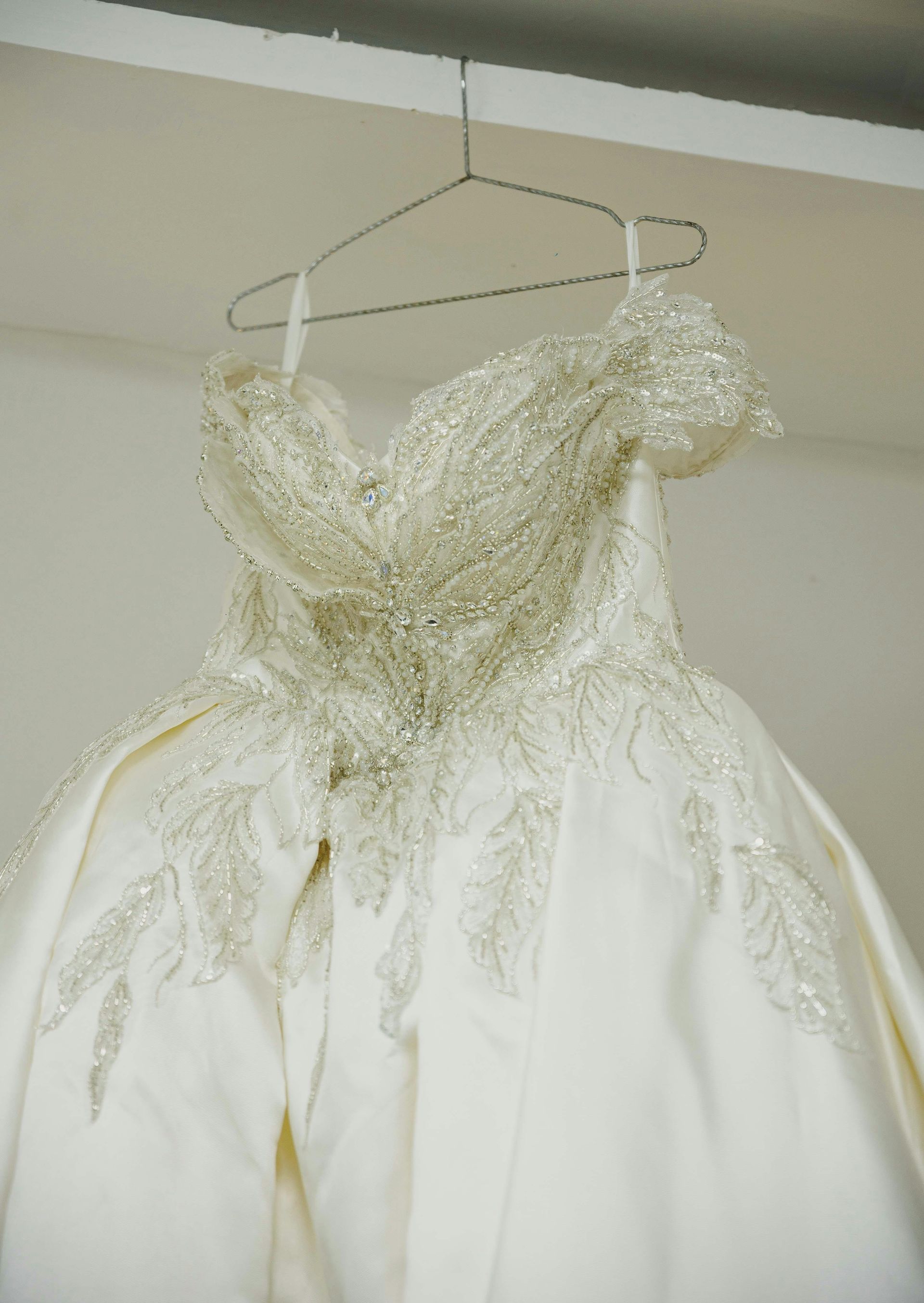A white, strapless ballgown with intricate silver beadwork on the bodice, hanging from a wire hanger.