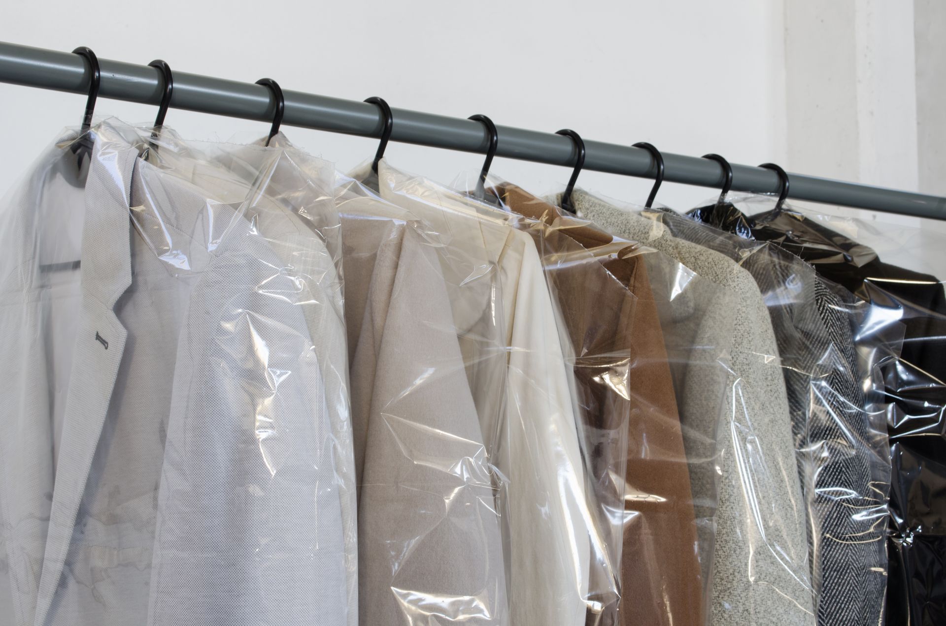 Several garments in clear plastic dry-cleaning bags hanging on a metal rack.