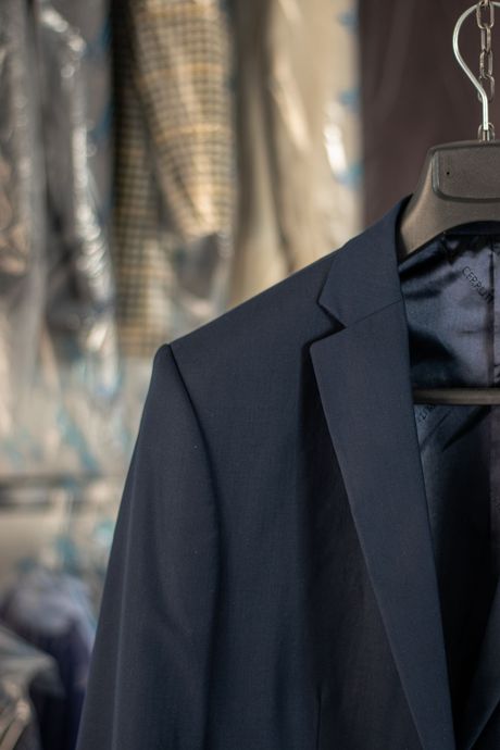 A close-up of a dark blue blazer hanging on a hanger against a blurred background of other garments.