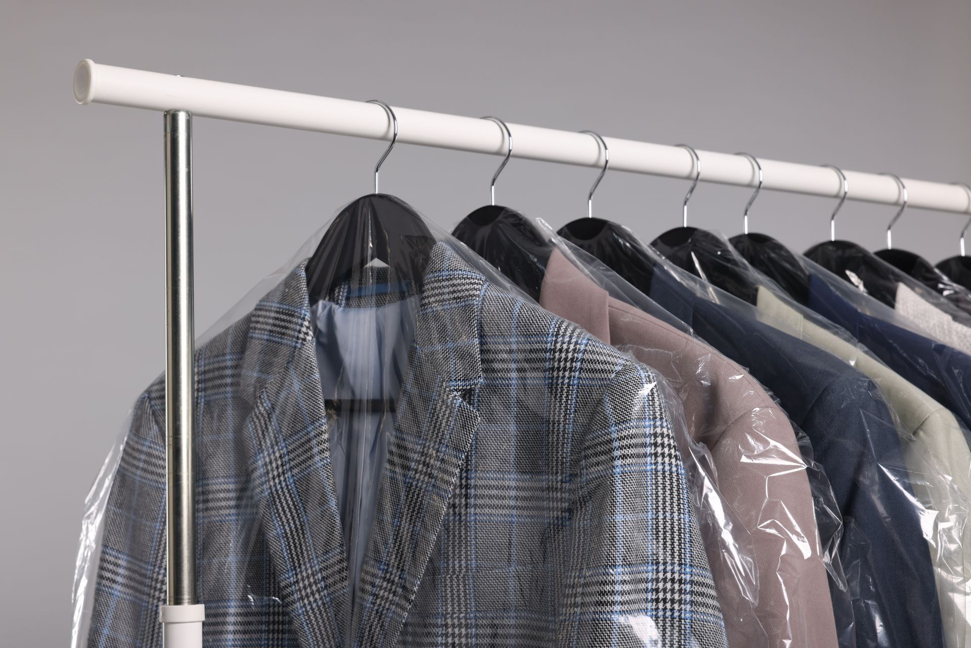 A row of suit jackets in protective plastic covers hanging on a rack against a plain gray background.