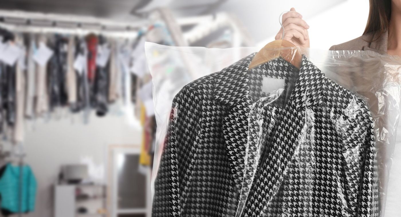 A person holds a black and white houndstooth blazer in plastic covering inside a dry cleaner shop.