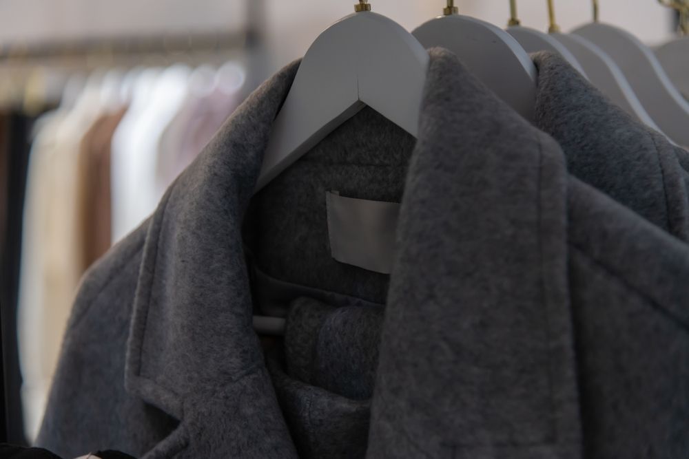 Dark gray coat hanging on a rack among other clothes