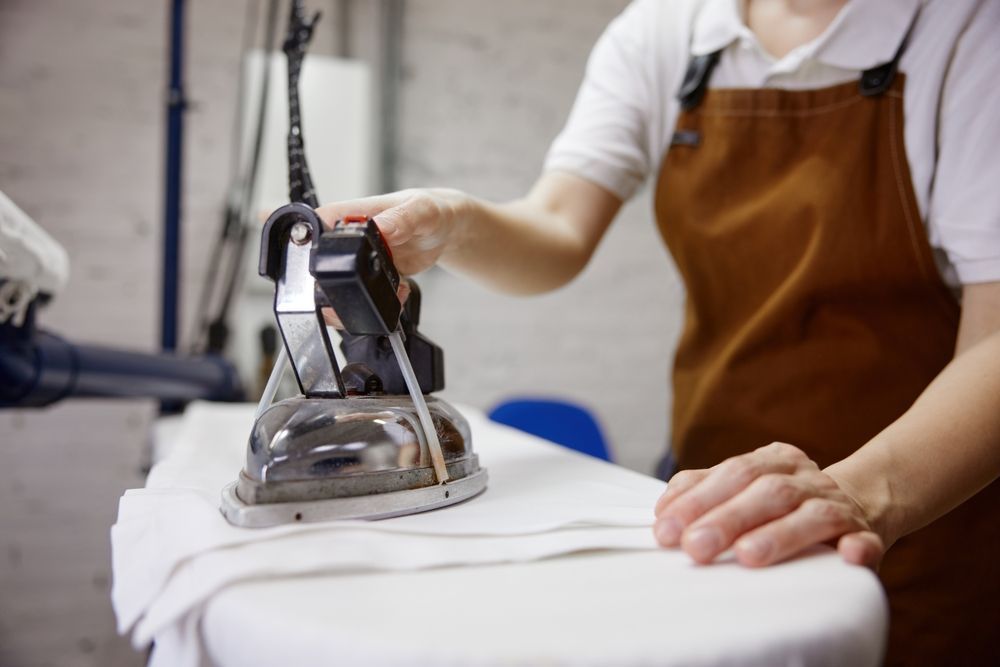 Person ironing white fabric in a workshop, wearing a brown apron
