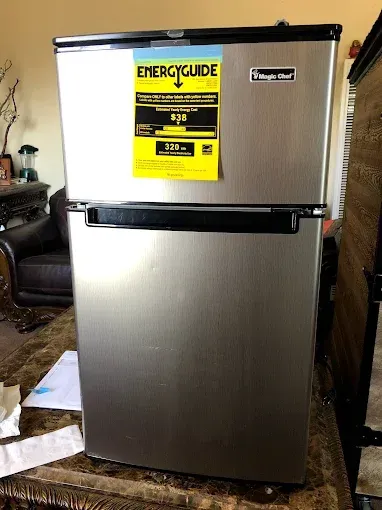 A stainless steel Magic Chef mini fridge with a freezer compartment and a yellow EnergyGuide label on the top door.