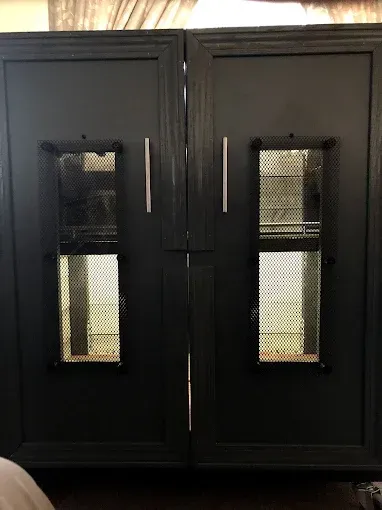 Two dark grey cabinet doors with silver handles, each featuring a centered, vertical window with a decorative metal mesh.