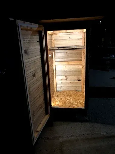An open, empty wooden cabinet with internal lighting, set against a dark background.