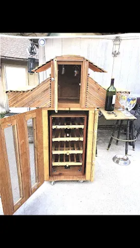 A wooden, tiered wine cabinet on wheels with a glass door, open shelves for bottles, and a top cupboard.