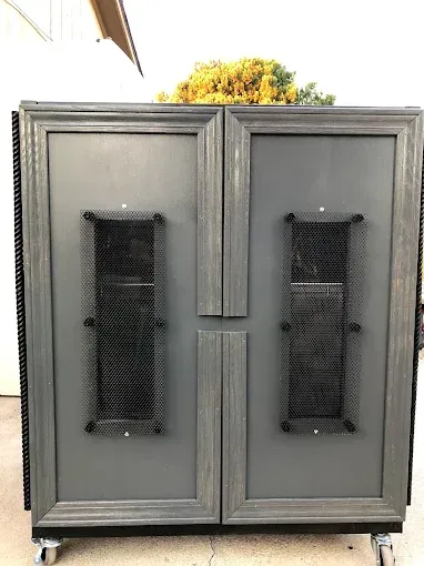 A gray, dual-door cabinet on wheels featuring vertical mesh panels and dark wood-toned framing.