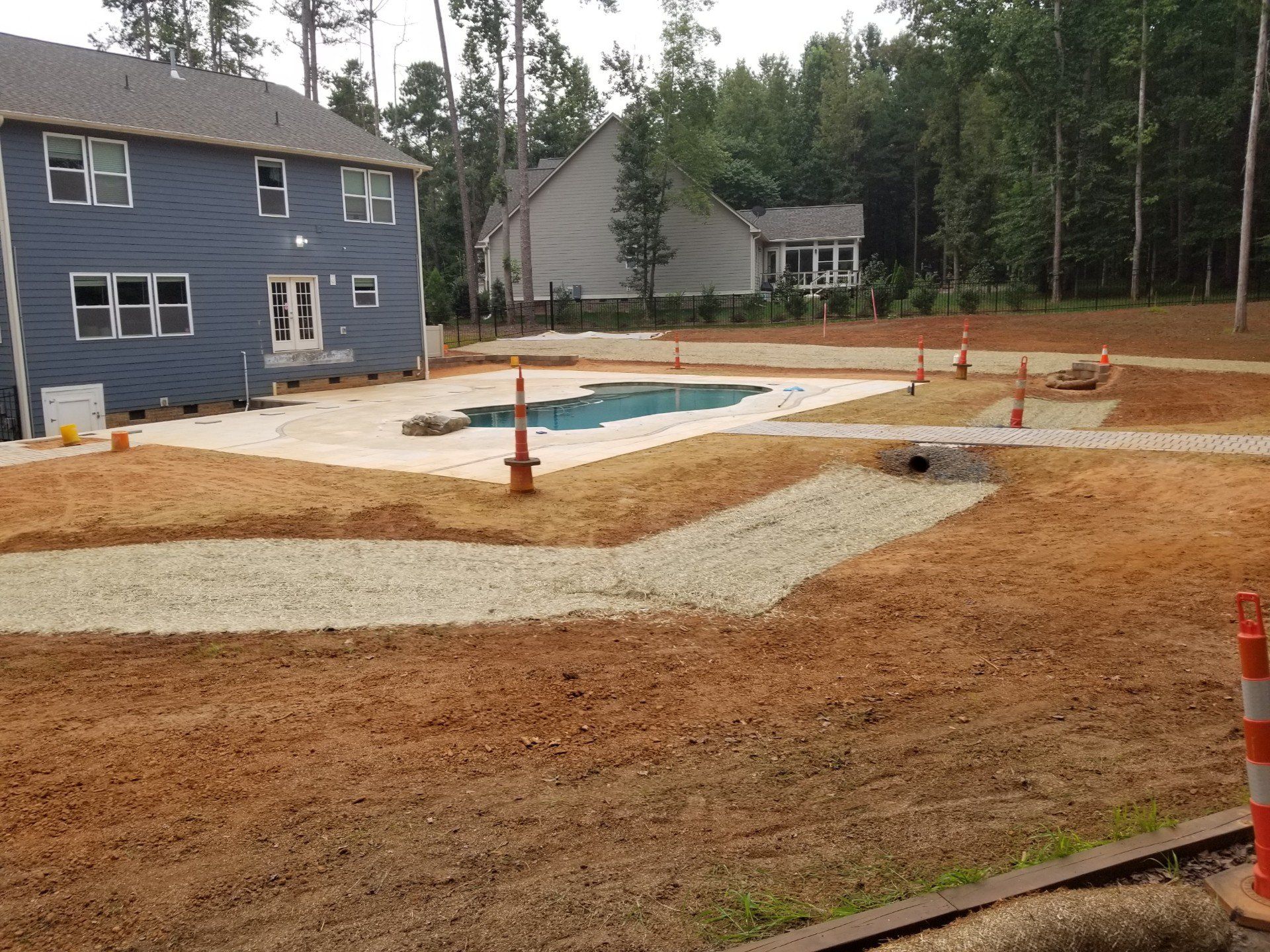 A blue house with a newly installed swimming pool and a dirt-covered backyard under construction.