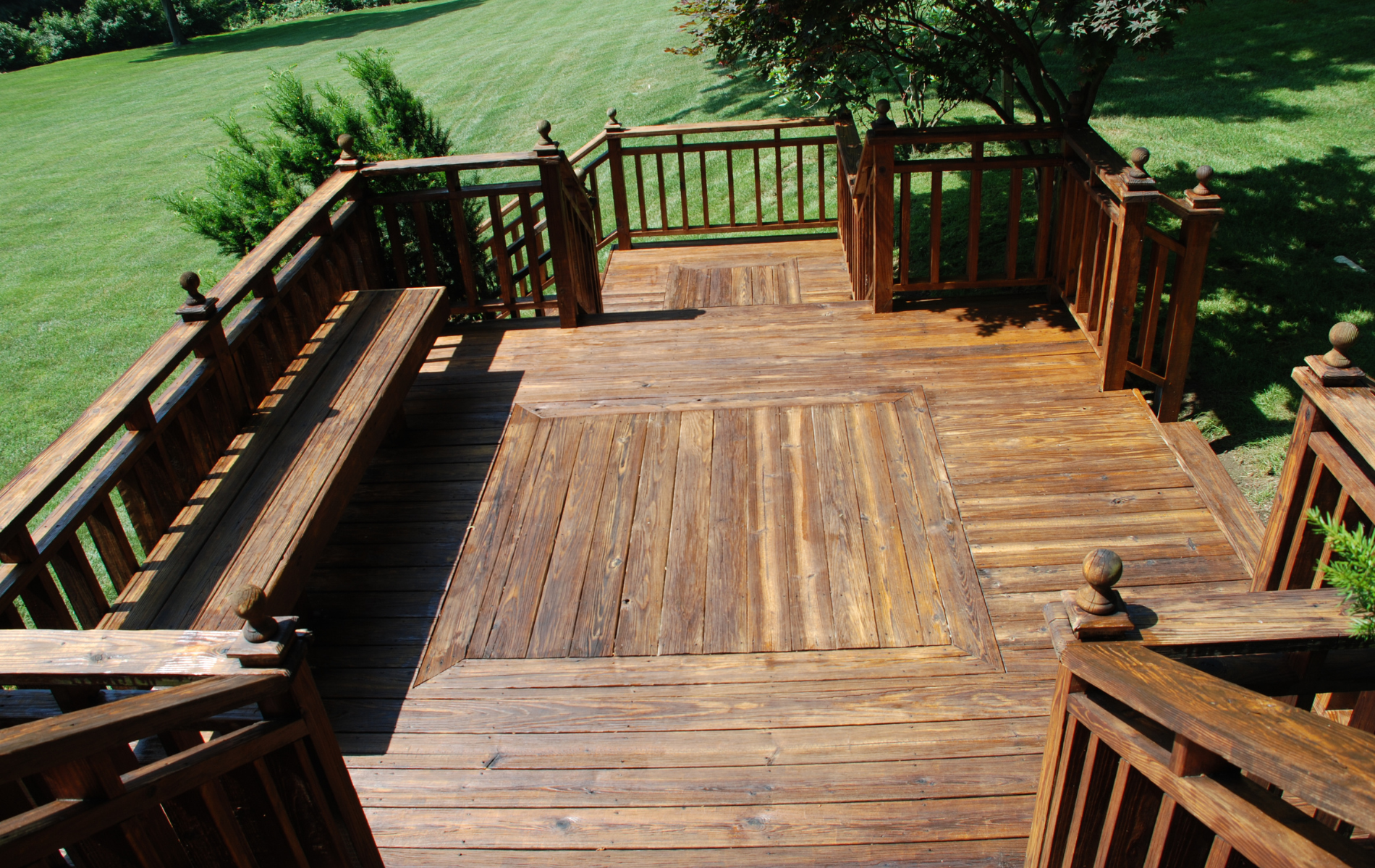 A high-angle view of a wooden deck with a built-in bench, decorative railing, and a central square patterned inlay.