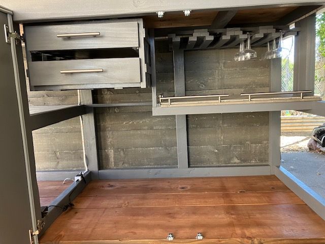 Interior view of a rustic grey wooden bar cabinet with two drawers, stemware storage, and an open lower shelf.