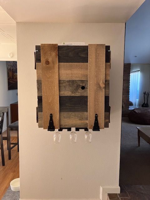 A rustic wooden wall-mounted wine rack with metal accents, holding three stemless glasses, against a white wall.