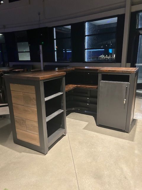 L-shaped bar counter with grey metal frames, wooden top and side panels, featuring open shelves and a cabinet door.