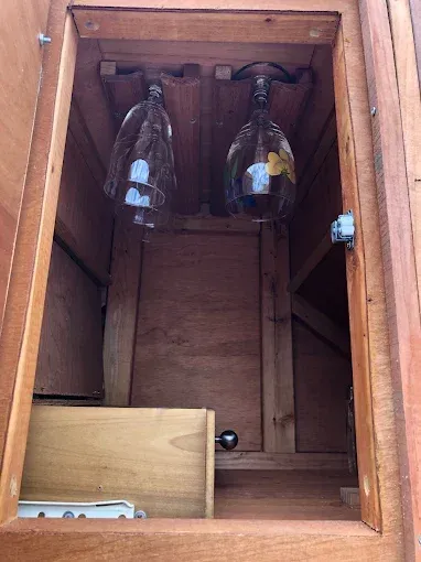 An open wooden cabinet with two wine glasses hanging from a rack and a small drawer at the bottom.