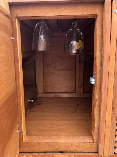 An open wooden cabinet with two hanging wine glasses inside.