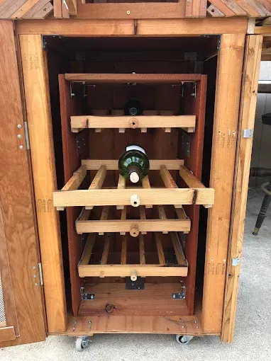 A custom wooden wine cabinet on wheels featuring several sliding bottle storage racks, one containing a wine bottle.