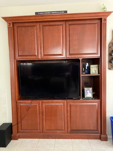 A large, built-in wooden entertainment center with upper and lower cabinets, a central TV, and side shelving.