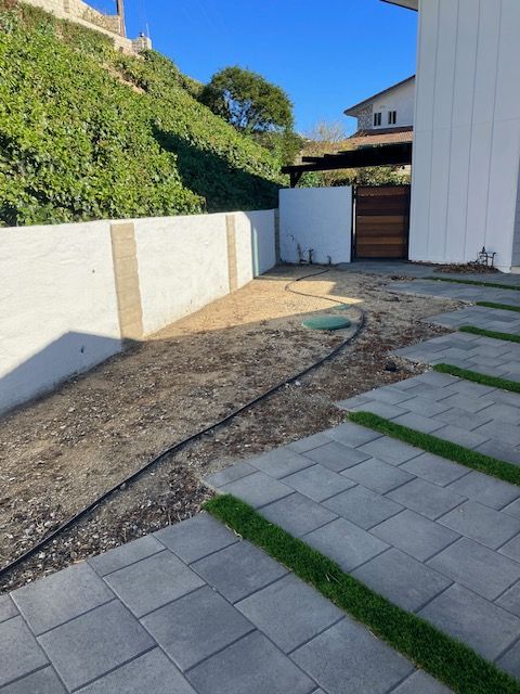 A modern home exterior with a stone paver path, a mulch side yard, a white retaining wall, and a wood-slatted gate.