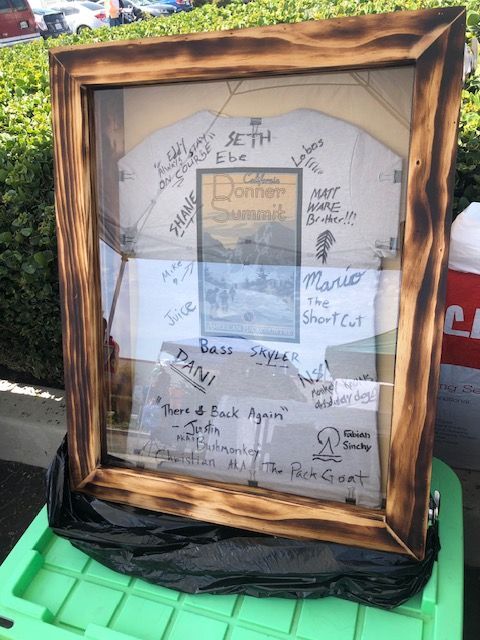 A signed, framed Donner Summit memento displayed in a shadow box atop a green plastic bin in an outdoor setting.