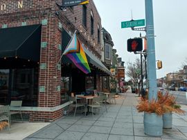 Street corner with a rainbow awning, outdoor cafe seating, and a “Billiards” sign on a brick building.
