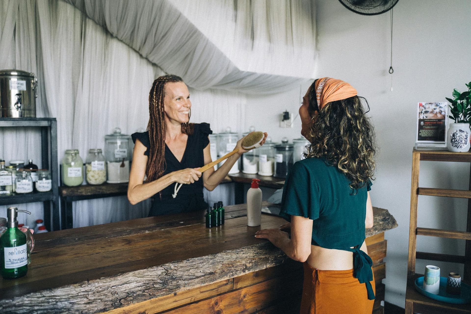 Two women chatting at a rustic café counter, one holding a bottle behind the bar.