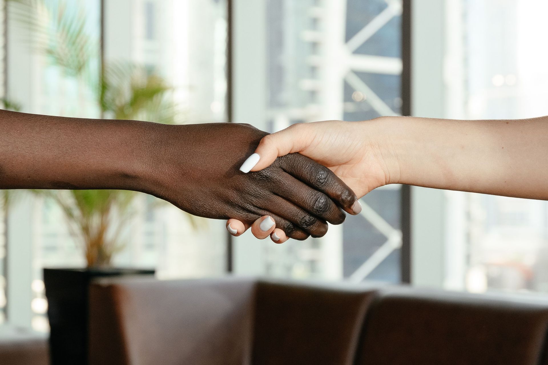 Two hands shaking in a bright indoor setting, one dark-skinned and one light-skinned.