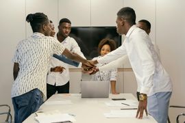Team members stack hands over a conference table during a meeting.