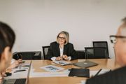 Business meeting with a woman speaking at a conference table, laptops and papers spread out