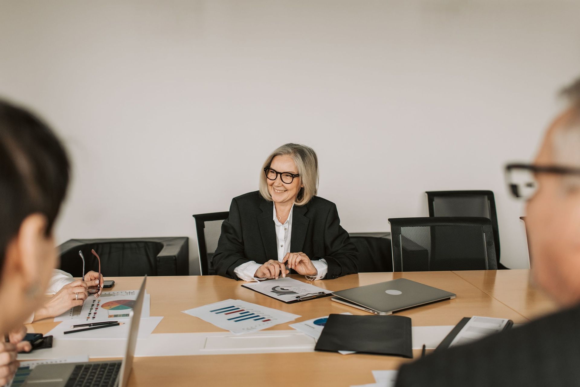 Business meeting with a woman speaking at a conference table, laptops and papers spread out