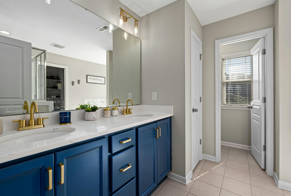 Blue vanity bathroom with double sinks, white countertop, and a view into a laundry area