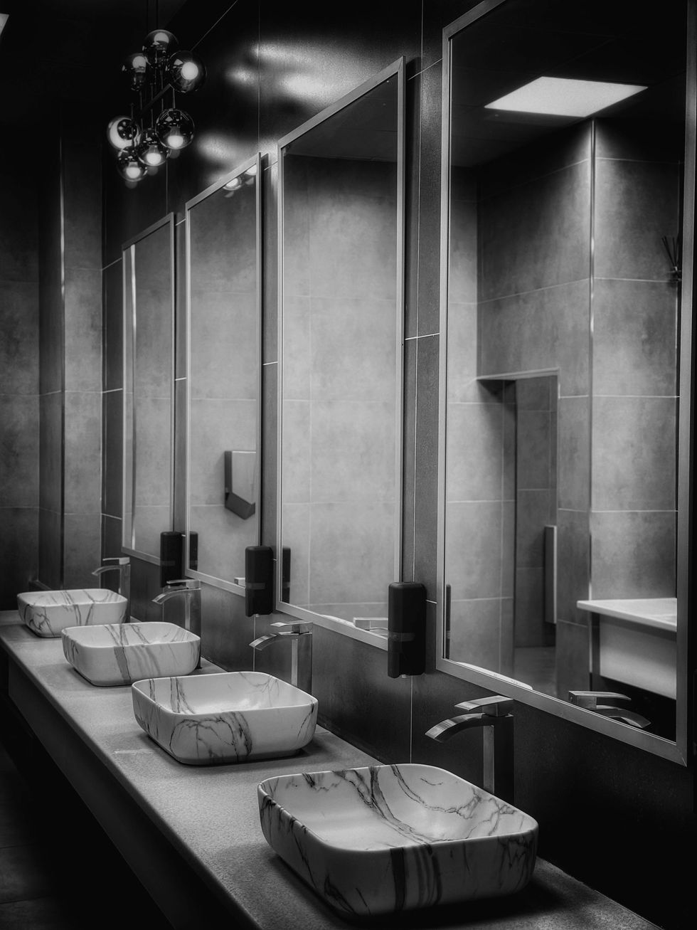 Modern restroom sinks with mirrors and overhead lights in black-and-white tones