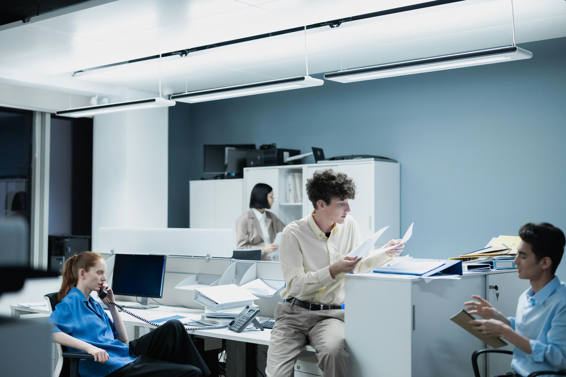 People collaborating in a modern office, discussing papers around desks under bright overhead lights