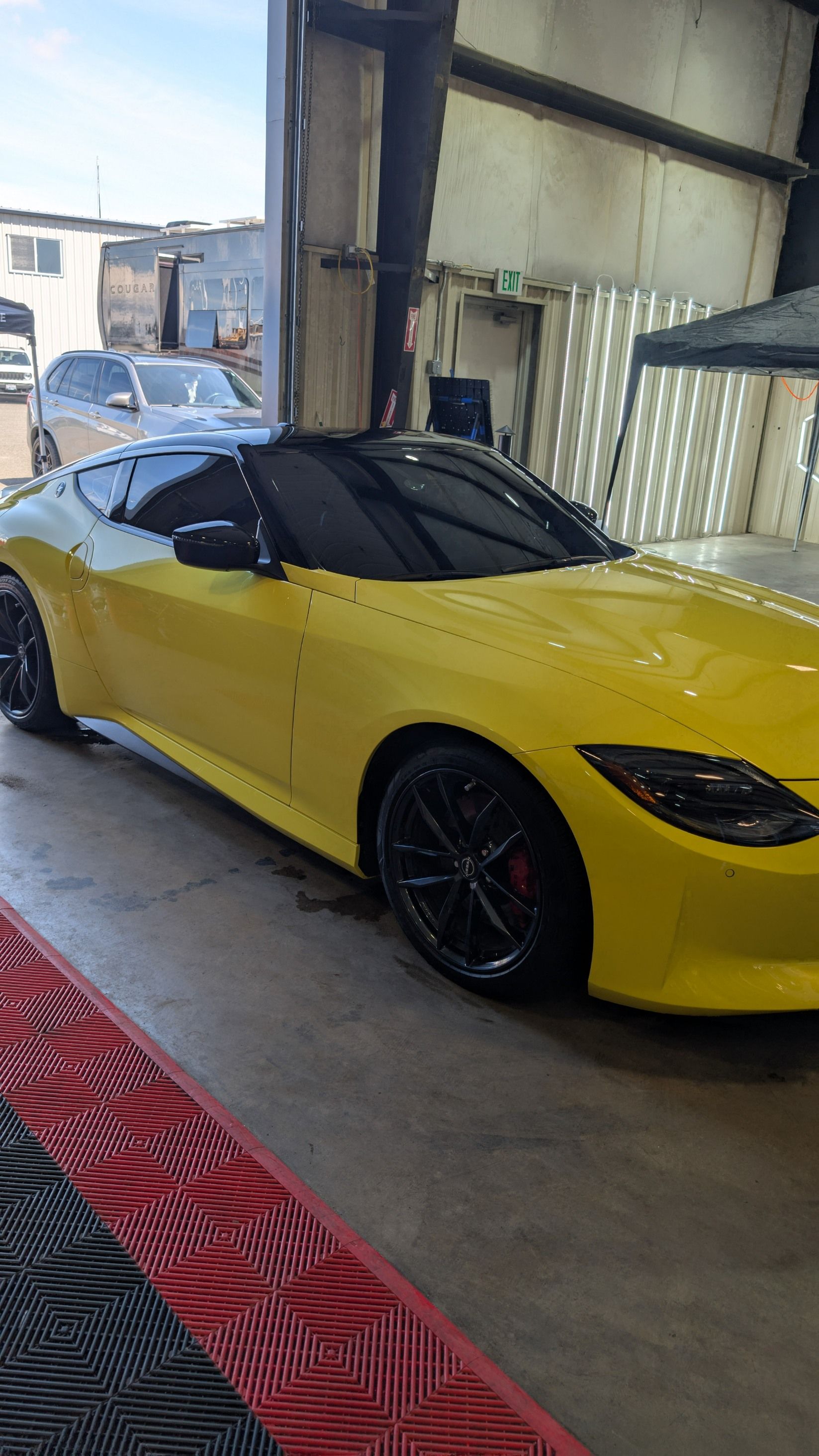 A bright yellow Nissan Z sports car parked inside an industrial garage with black wheels and tinted windows.
