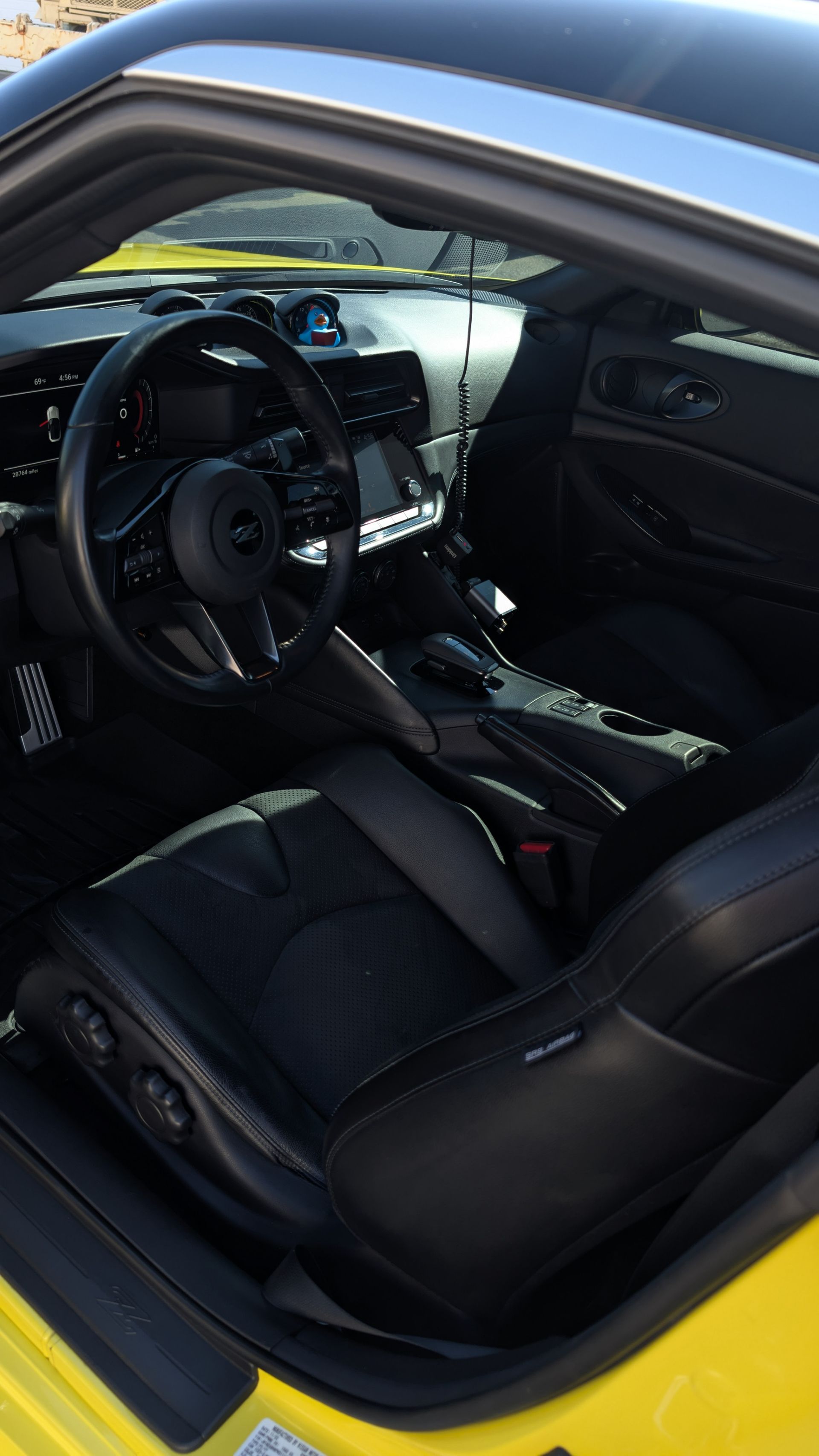 Interior view of a modern yellow sports car showing the black leather driver's seat, steering wheel, and dashboard.