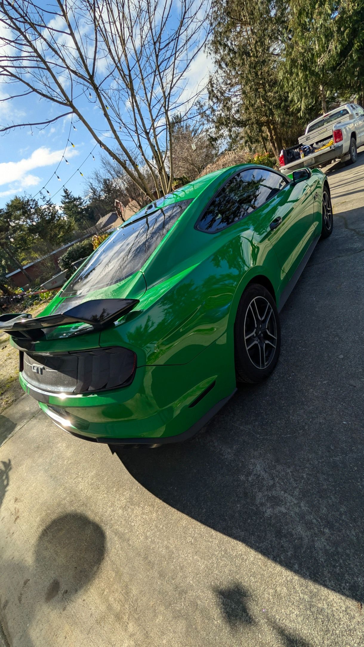 A bright green Ford Mustang parked on an asphalt driveway on a sunny day with trees in the background.