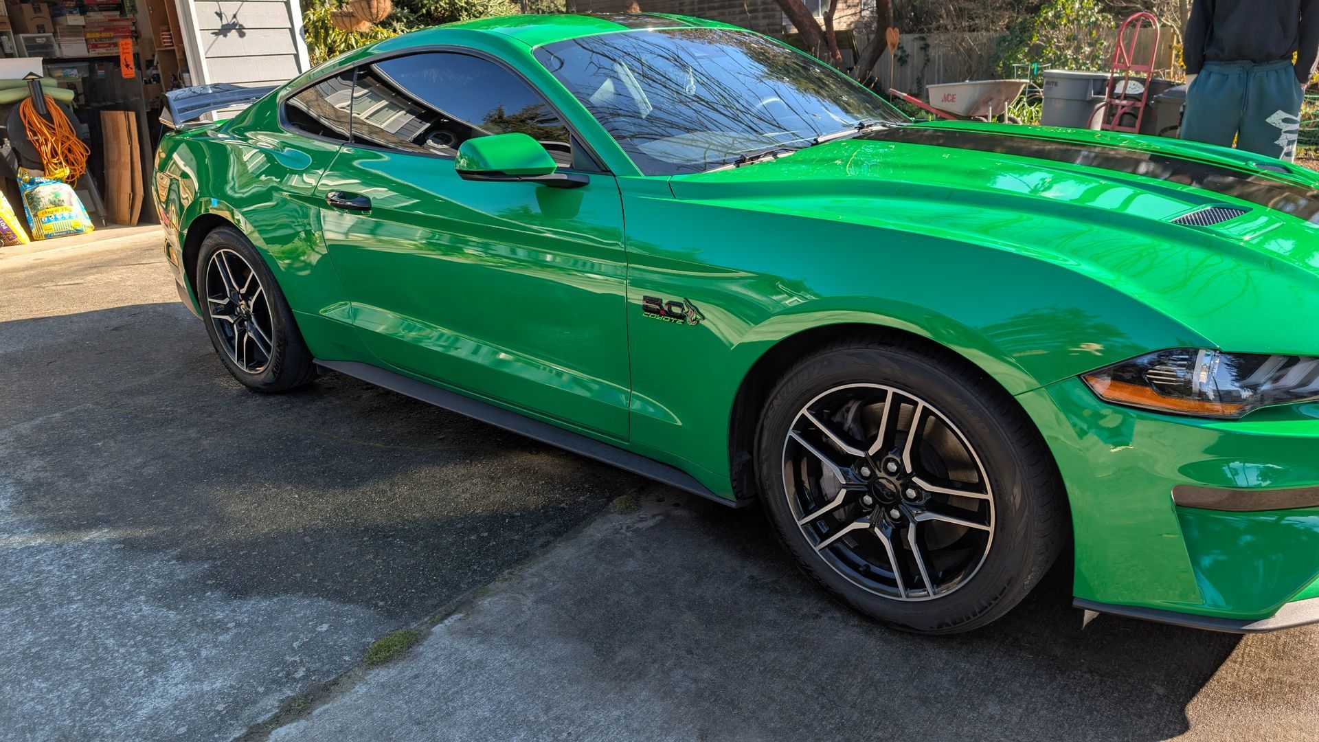 A bright green Ford Mustang parked on an asphalt driveway during the day.