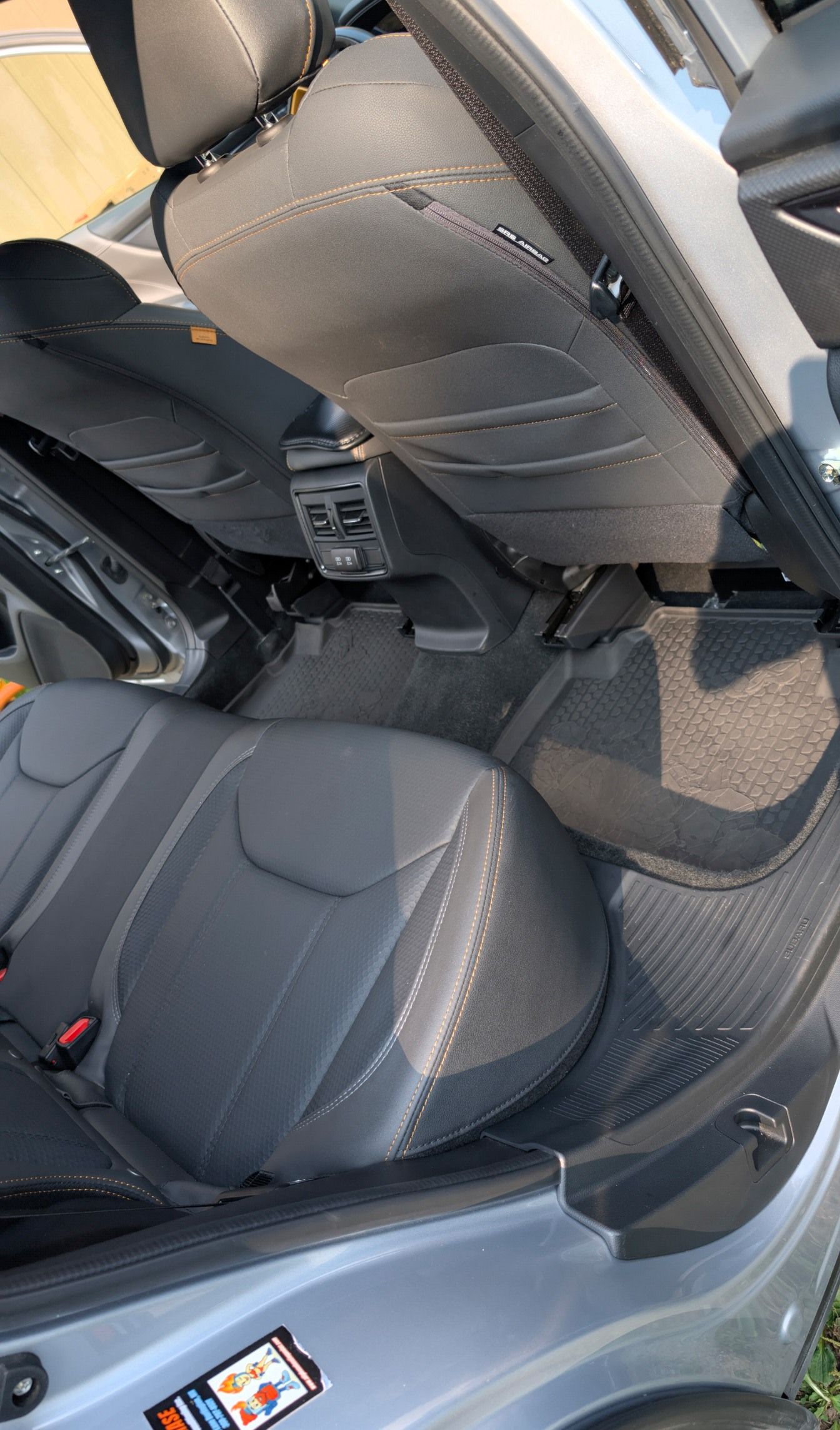 A high-angle view of a car's back interior showing black leather seats, a central console, and grey floor mats.