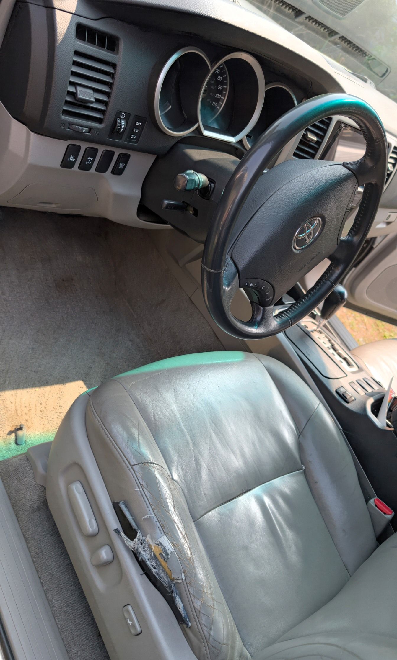 A car's interior featuring a grey leather driver seat with visible wear and a steering wheel with a Toyota emblem.
