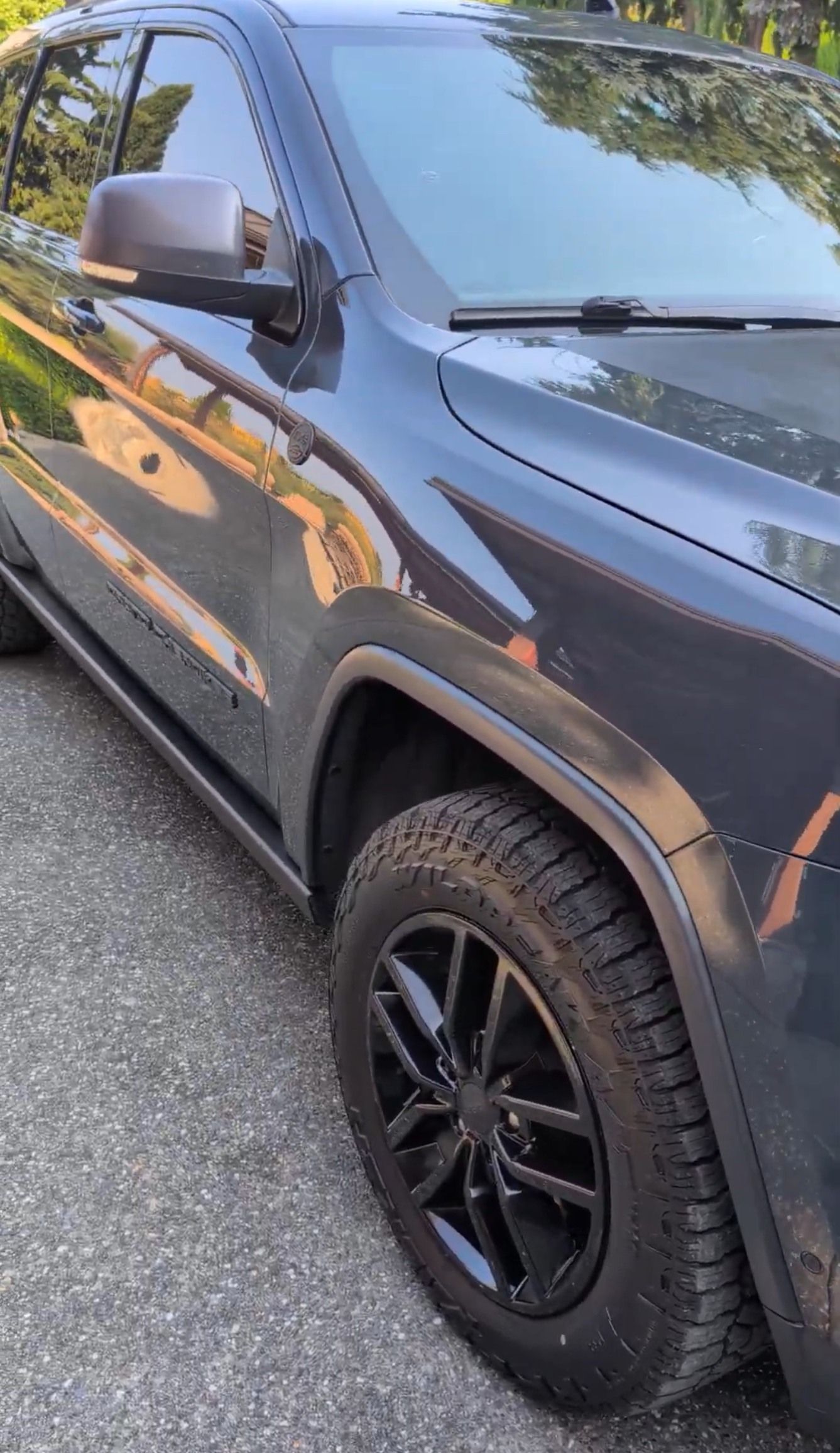 A side-angle view of a dark grey SUV parked on an asphalt surface, highlighting its black wheel and tire.