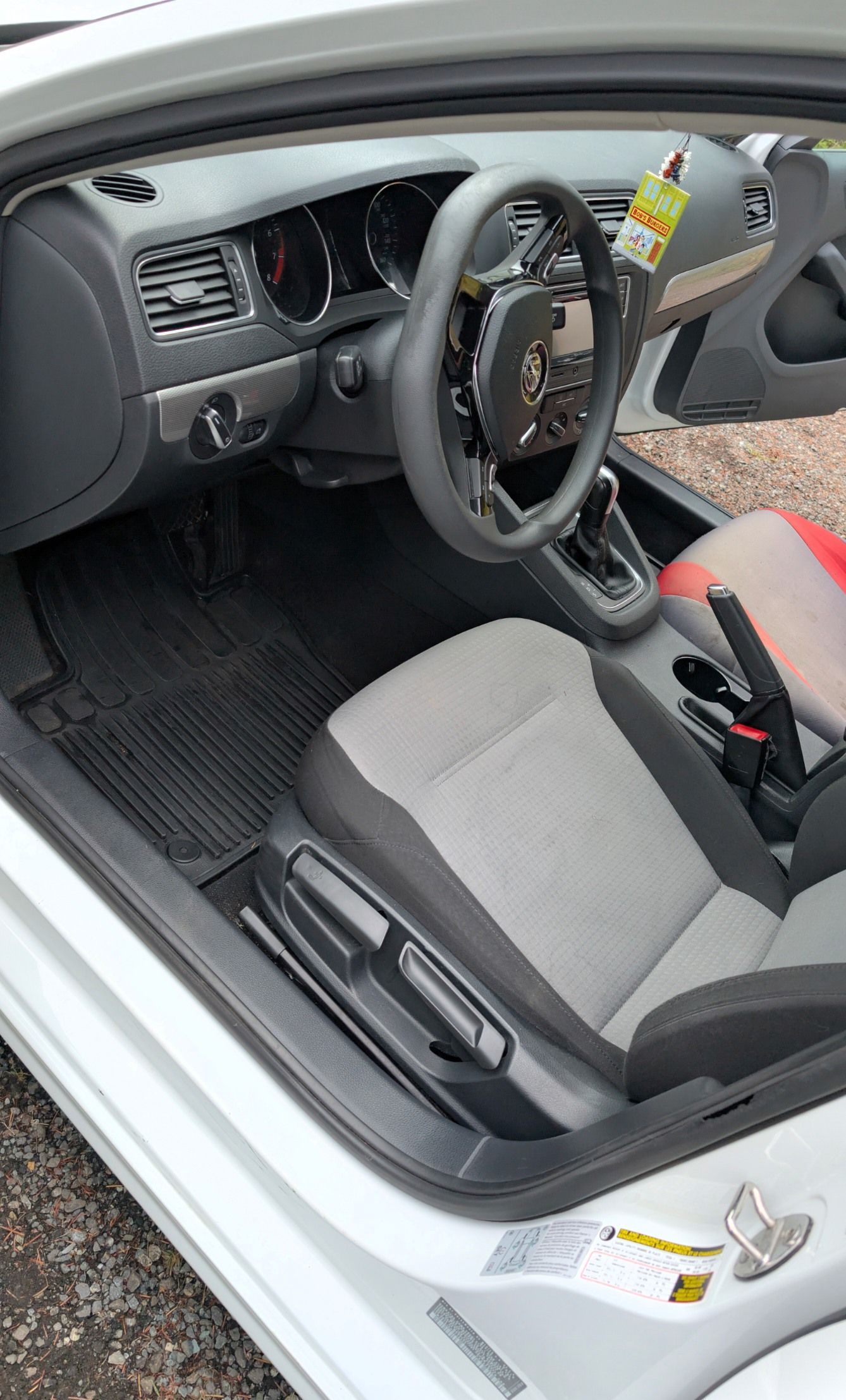 Interior of a light-colored vehicle with a black dashboard, steering wheel, and gray-and-black fabric bucket seats.